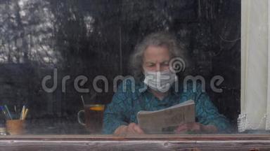 <strong>年迈</strong>的老年妇女戴着面具，坐在家里看报纸。 检疫。 呆在家里。 冠状病毒仍然是